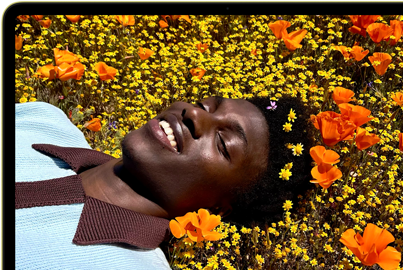 MacBook Neo, couleur jaune agrume, écran affichant une personne souriante allongée dans un champ de fleurs ensoleillé