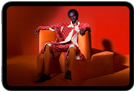 iPad mini, vue de face, écran affichant une image éclatante d’une personne portant un costume orange, assise sur une chaise orange, dans une pièce orange