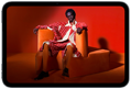 iPad mini, vue de face, écran affichant une image éclatante d’une personne portant un costume orange, assise sur une chaise orange, dans une pièce orange