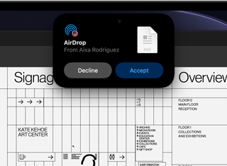 L’écran affiche la Dynamic Island avec une demande AirDrop dans une petite fenêtre au-dessus d’un fichier Adobe Acrobat ouvert