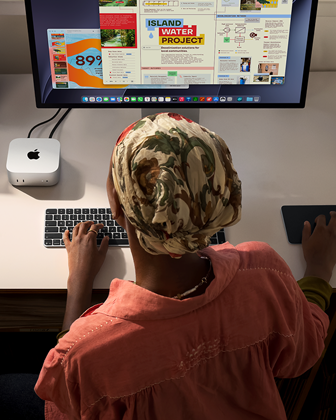 Une personne assise à un bureau utilise un Mac mini connecté à un Studio Display, Magic Keyboard, Magic Trackpad, divers objets