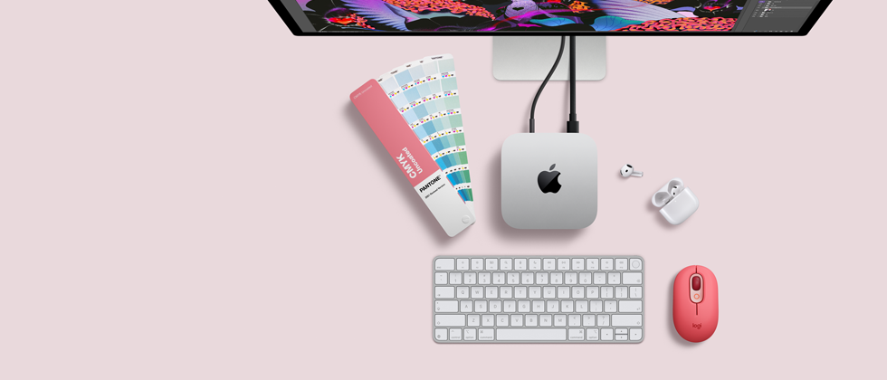 Mac mini, dessus, aluminium argent, angles arrondis, logo Apple noir brillant centré, connecté par un câble, Studio Display partiellement visible en haut, AirPods 4, boîtier ouvert, pastilles de couleur Pantone, et clavier et souris Logitech rouges