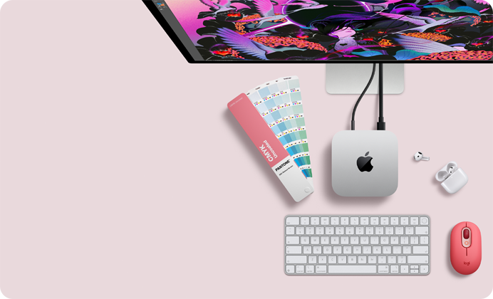 Mac mini, dessus, aluminium argent, angles arrondis, logo Apple noir brillant centré, connecté par un câble, Studio Display partiellement visible en haut, AirPods 4, boîtier ouvert, pastilles de couleur Pantone, et clavier et souris Logitech rouges
